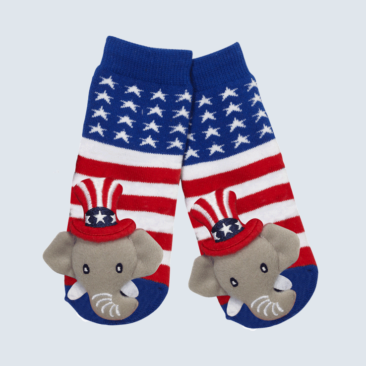 Two socks against a white background. The socks feature an American flag pattern and a cute plush elephant charm on the toe.