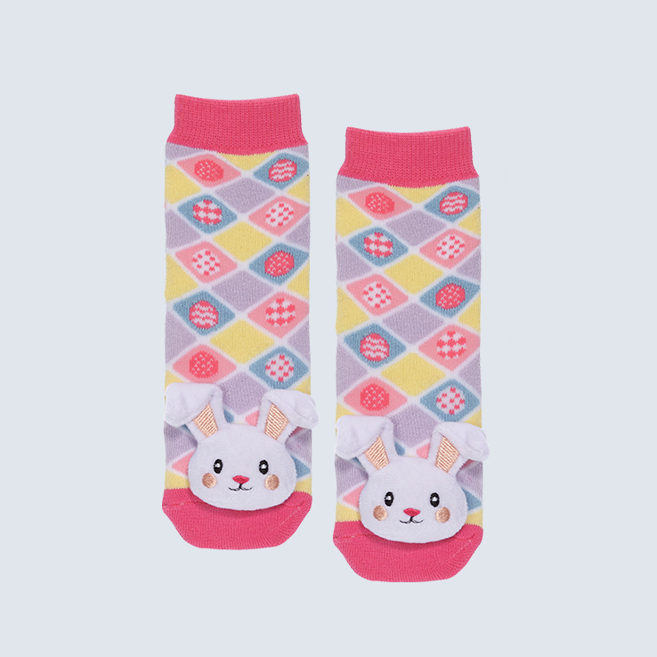 Two pink bunny socks against a white background. The socks feature pink, purple, blue, and yellow diamond motifs and a cute plush bunny charm on each toe.
